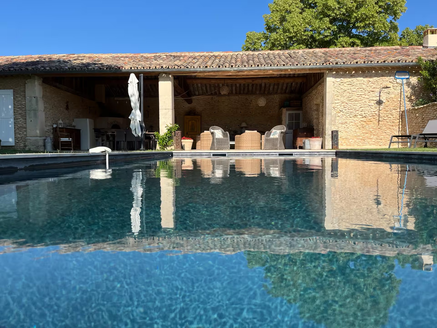 Mas en pierre vu depuis la piscine avant retouche, deux fauteuils rotin sous l'auvent