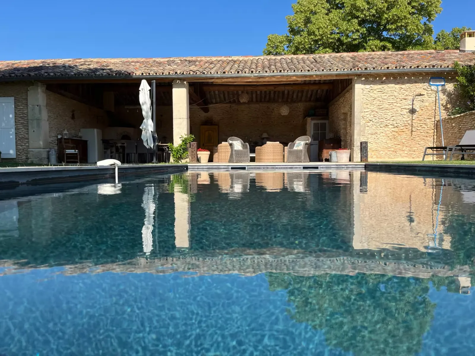 Mas en pierre vu depuis la piscine avant retouche, deux fauteuils rotin sous l'auvent